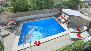 Une piscine entourée d’un mur de pierre et de verdure, avec des chaises longues et des parasols.