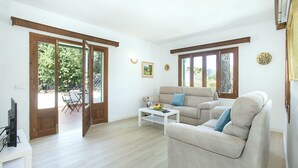 Un salon spacieux avec un canapé beige, une table basse blanche et un téléviseur posé sur un meuble.