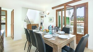 Un coin repas avec une table en bois dressée pour quatre personnes, des chaises noires et une vue sur l’extérieur grâce à de grandes fenêtres.