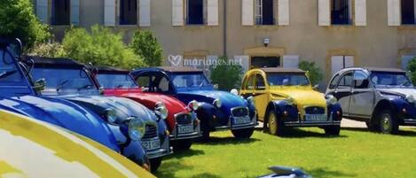 A row of vintage cars parked in front of a building with a tiled roof and white shutters.