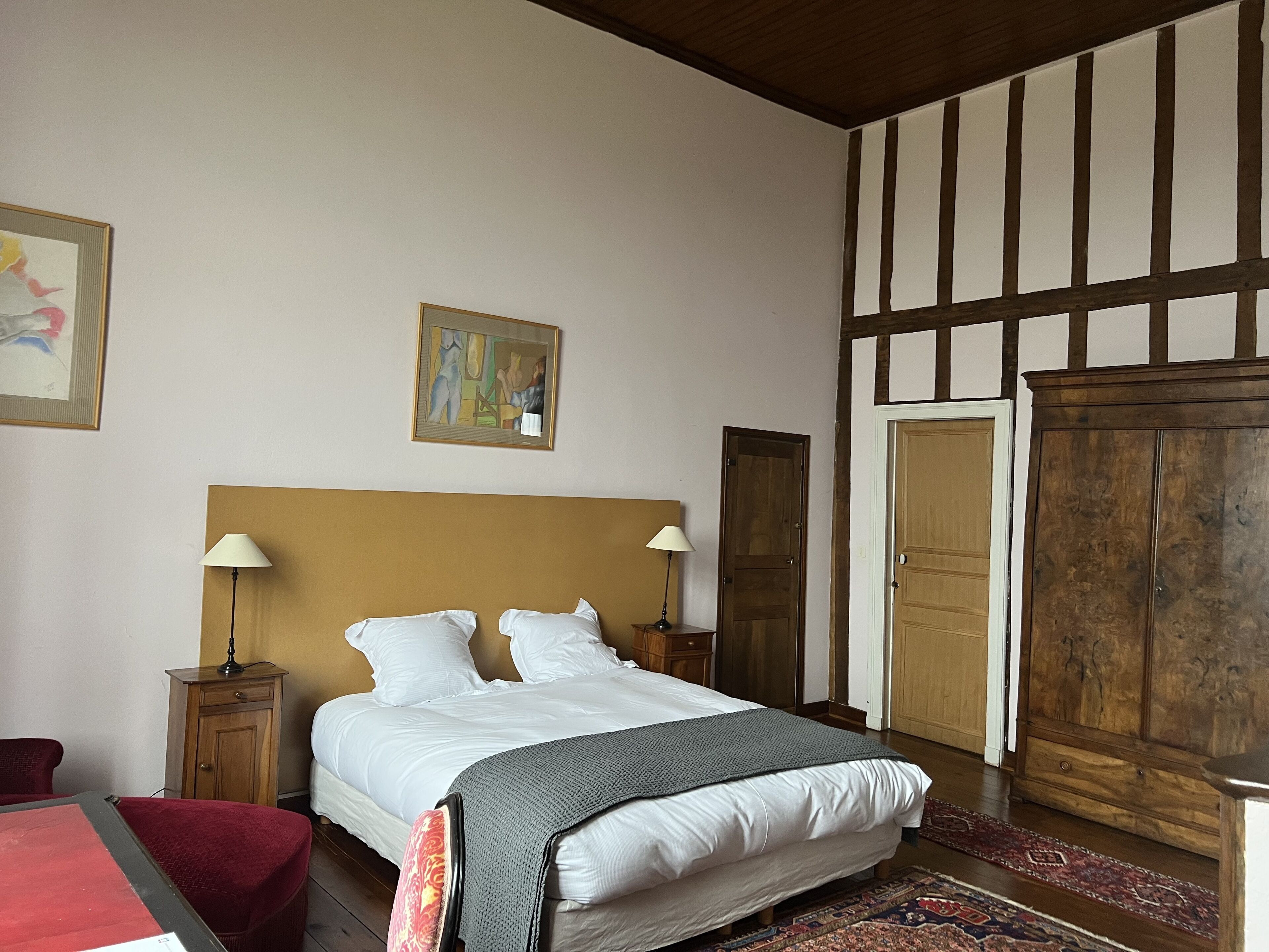Une chambre à coucher avec un grand lit, deux tables de chevet avec des lampes, une armoire en bois et un fauteuil rouge.