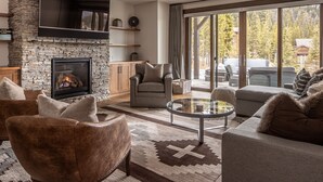Ein modernes Wohnzimmer mit Kamin aus Stein, Ledersofas, einem Glastisch und einer großen Schiebetür zu einer Außenpatio.