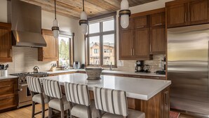 Eine moderne Küche mit Holzschränken, Edelstahlgeräten und einer großen Kochinsel mit Barhocker.