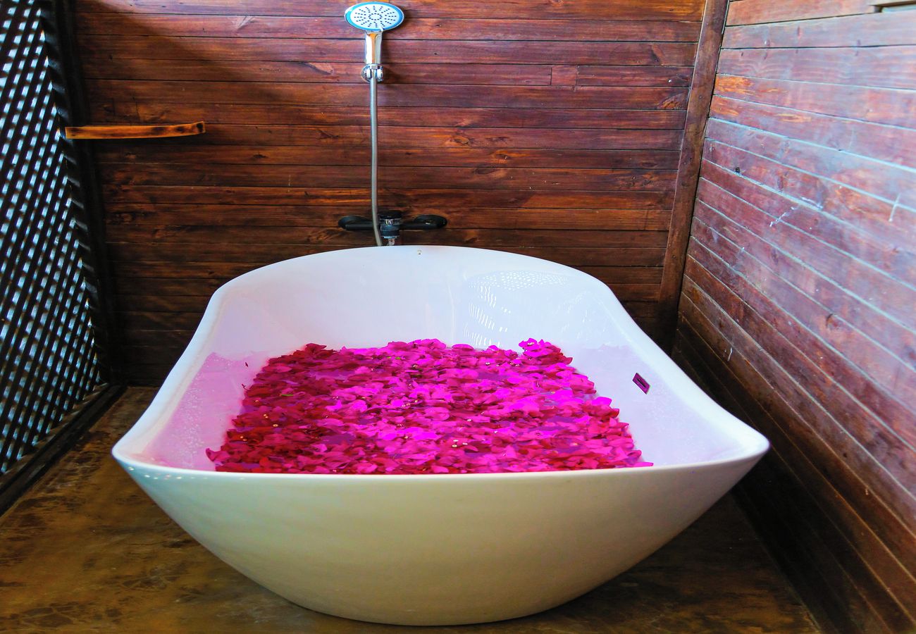 A bathtub filled with pink bath products, a wooden wall, and a showerhead.