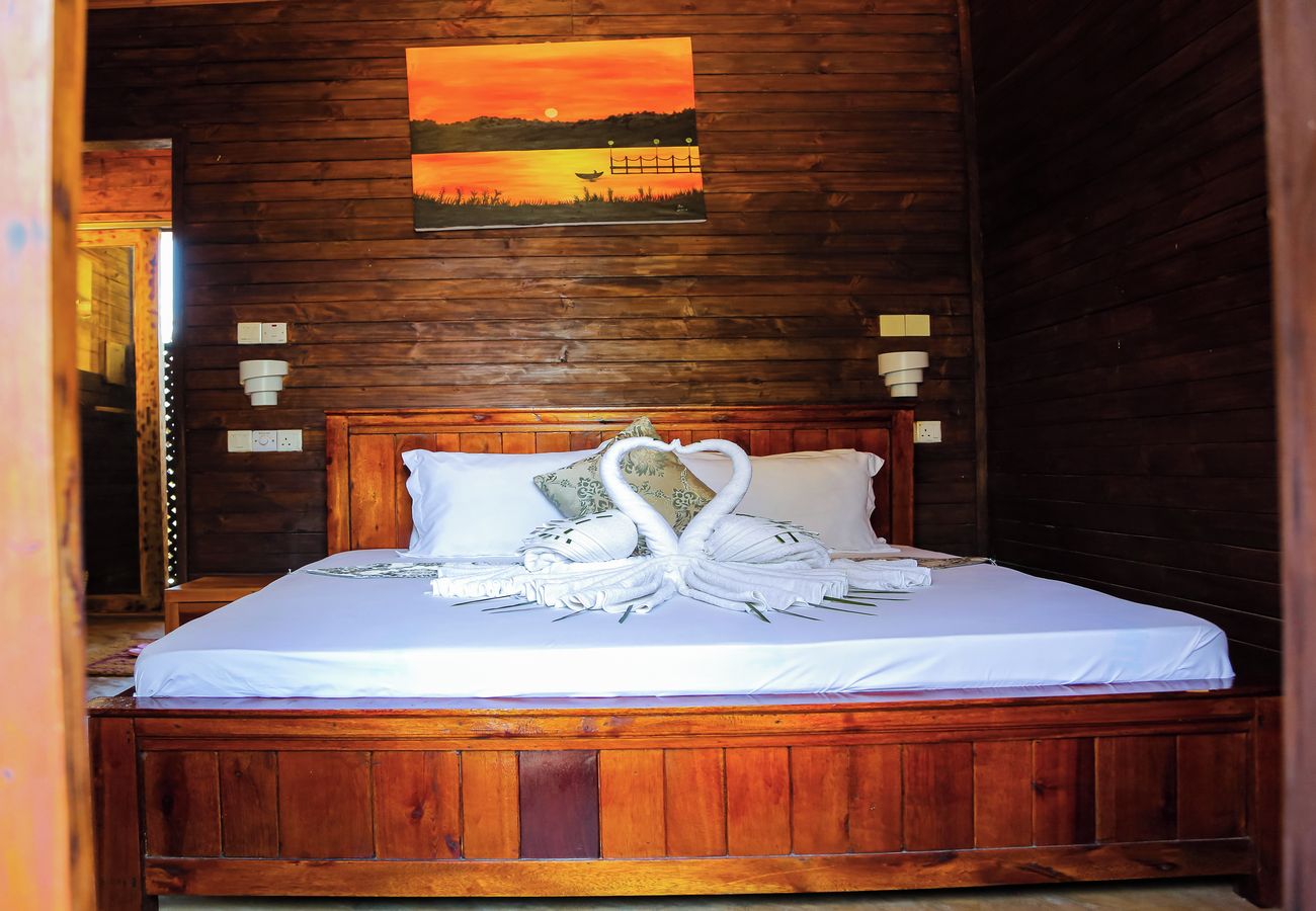 A wooden-framed room with a bed, a painting of a sunset, and a swan-shaped towel arrangement.