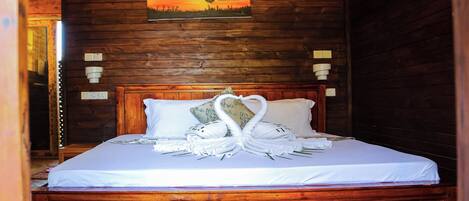 A wooden-framed room with a bed, a painting of a sunset, and a swan-shaped towel arrangement.
