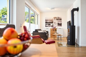 A modern living room with a sofa, a red chair, a table with fruit, and a black wood stove.