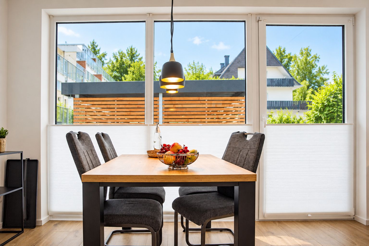 Un comedor con una mesa de madera, cuatro sillas, un frutero y una lámpara colgante.
