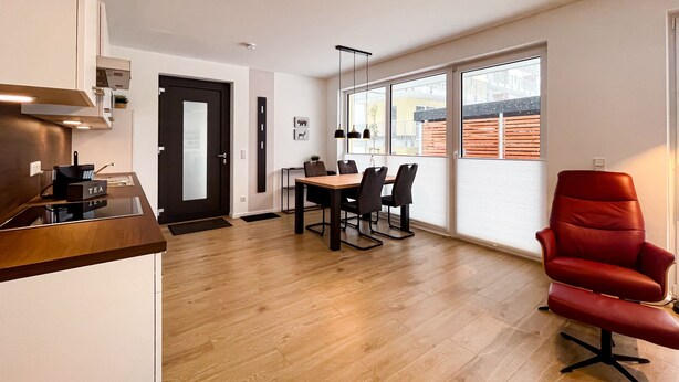 A modern kitchen with a built-in tea station, a dining area with a wooden table and chairs, and a large window with a view of a wooden deck. - Modern vacation apartment for 4 people in the best city location (Winterberg)