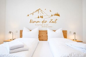 Ein Hotelzimmer mit einem Bett, zwei Nachttischen mit Lampen, einem hölzernen Kopfteil und einer Wanddekoration mit einer Berglandschaft und Text.