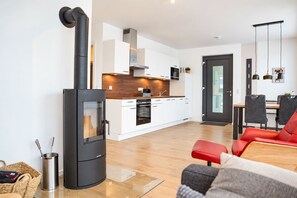 A modern kitchen with white cabinets, a built-in oven, and a black stove. There is a dining area with a table and chairs, and a red sofa in the foreground.