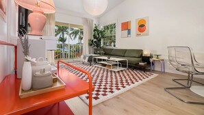 A modern living room with a sofa, coffee table, and a red chair. There is a large window with a view of palm trees.