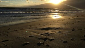 A beach with footprints leading to the water, waves, and a sunset.