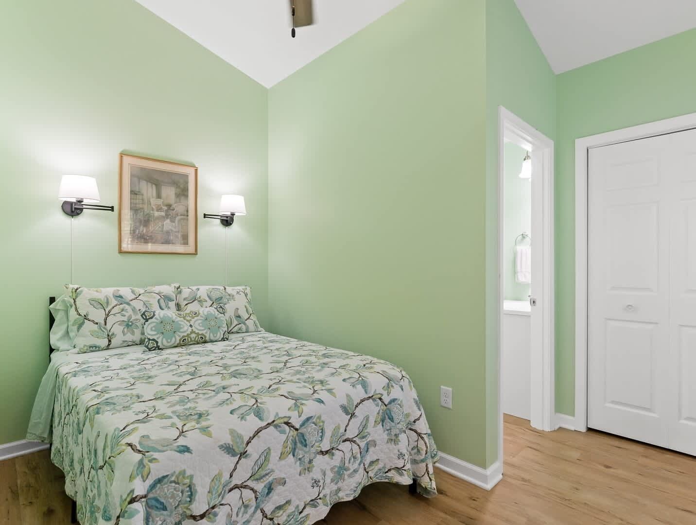 A bedroom with a bed, two wall-mounted lamps, a framed picture, and a white door.