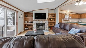 Een woonkamer met een stenen openhaard, een leren bank, houten planken en een televisie.