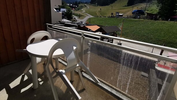 A balcony with a table and chairs, overlooking a mountain landscape with a ski resort in the distance. - Cozy studio at the foot of the slopes with balcony, TV and ski locker (Les Adrets-Prapoutel)