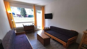 A room with a sofa, a wooden table, and a television mounted on the wall. - Cozy studio at the foot of the slopes with balcony, TV and ski locker (Les Adrets-Prapoutel)
