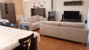 A living room with a sofa, TV, and a fireplace. There is a dining area with a table and chairs. - Family eco-cottage with garden, near hiking trail (Mesples)