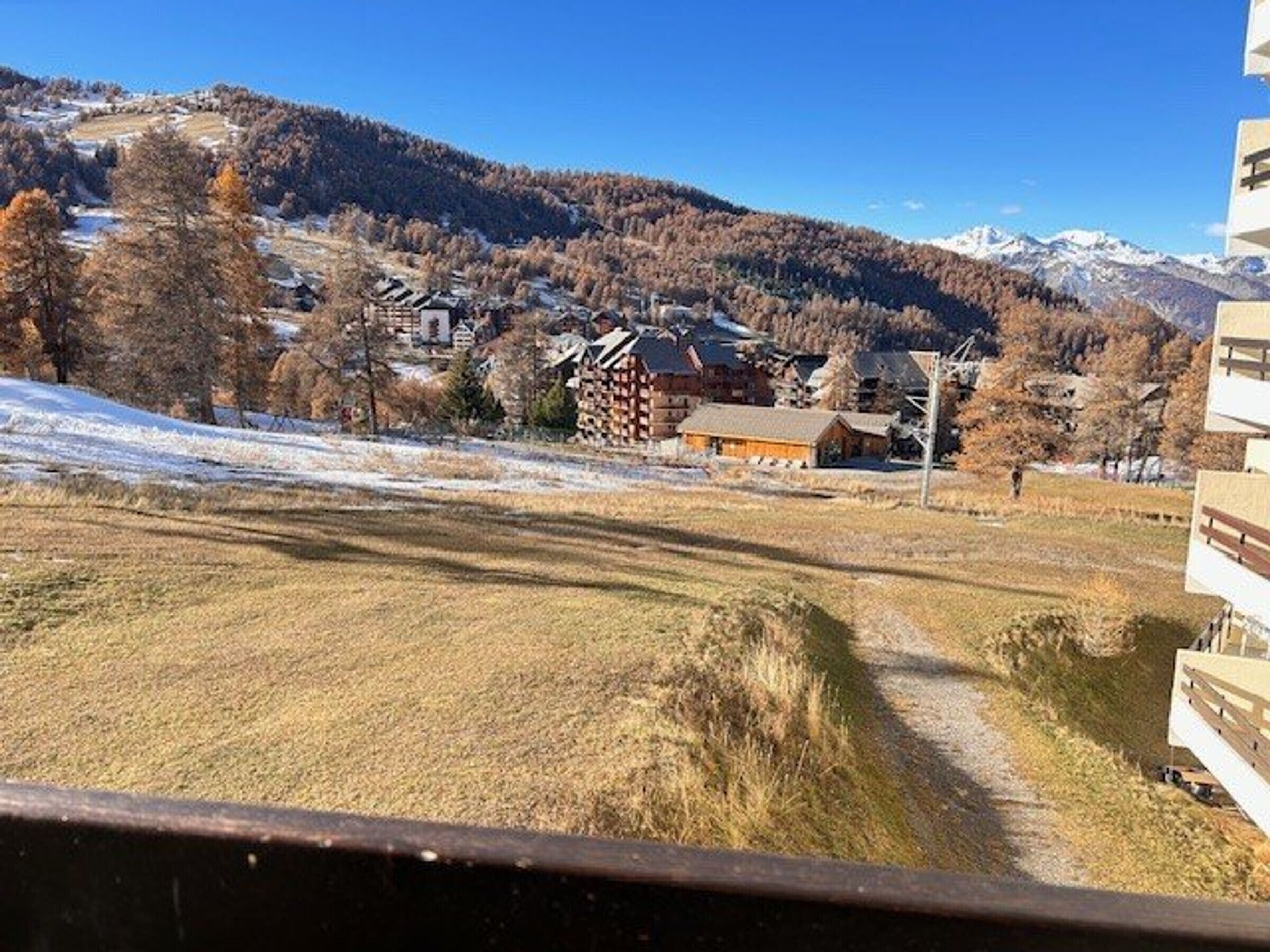 A rural village with traditional buildings, a clear sky, and snow-capped mountains in the background.