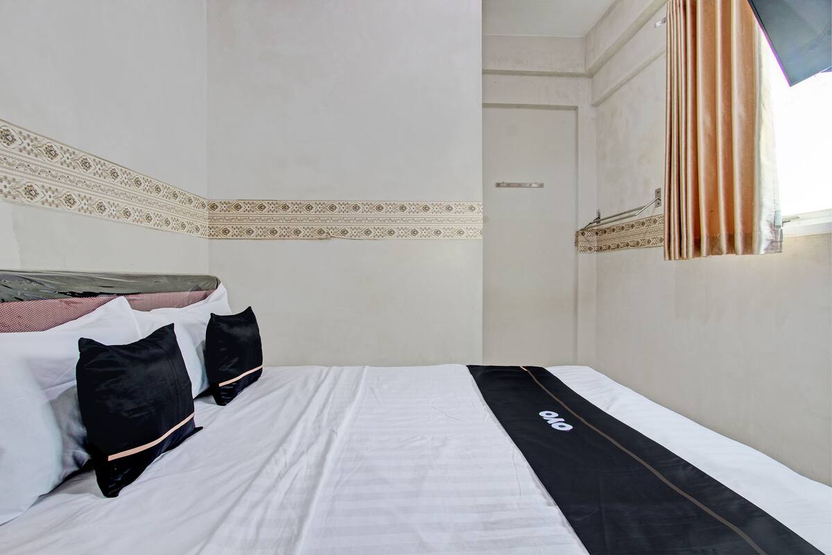 A hotel room with a neatly made bed, a decorative wall border, and a window with curtains.