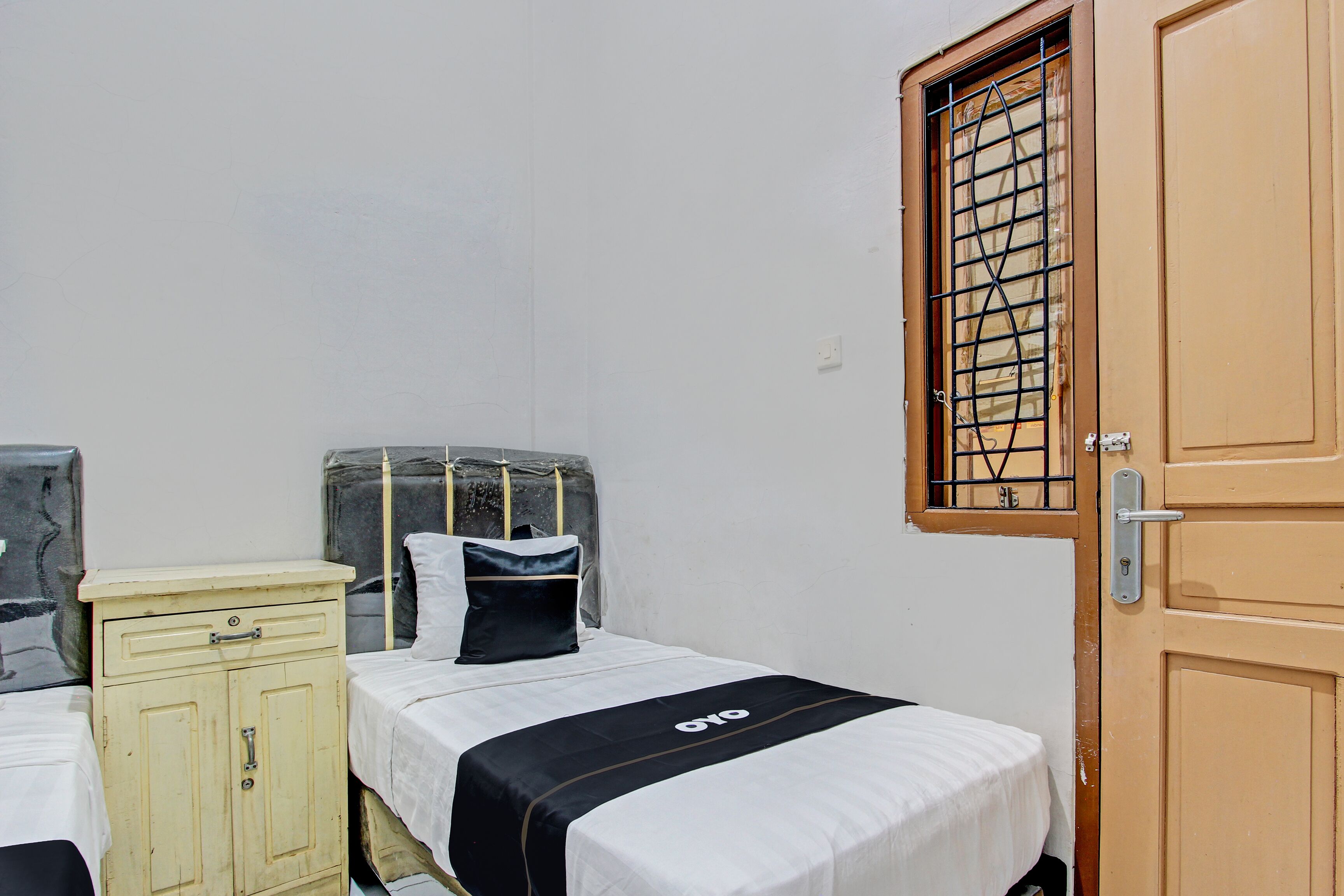 A small, compact bedroom with a single bed, a wooden wardrobe, and a window with bars.