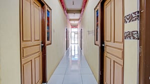 A corridor with wooden doors and tiled flooring, leading to a bright room with a view. - Capital O 93361 Dynasty Inn Syariah (Pekalongan)
