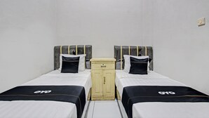 A room with two beds, each with a black and white bedspread and matching pillows. There is a small wooden cabinet between the beds. - Capital O 93361 Dynasty Inn Syariah (Pekalongan)