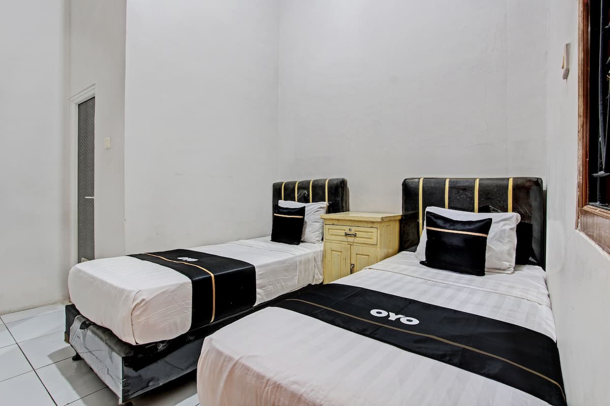 A small, clean room with two beds, a wooden nightstand, and a door.