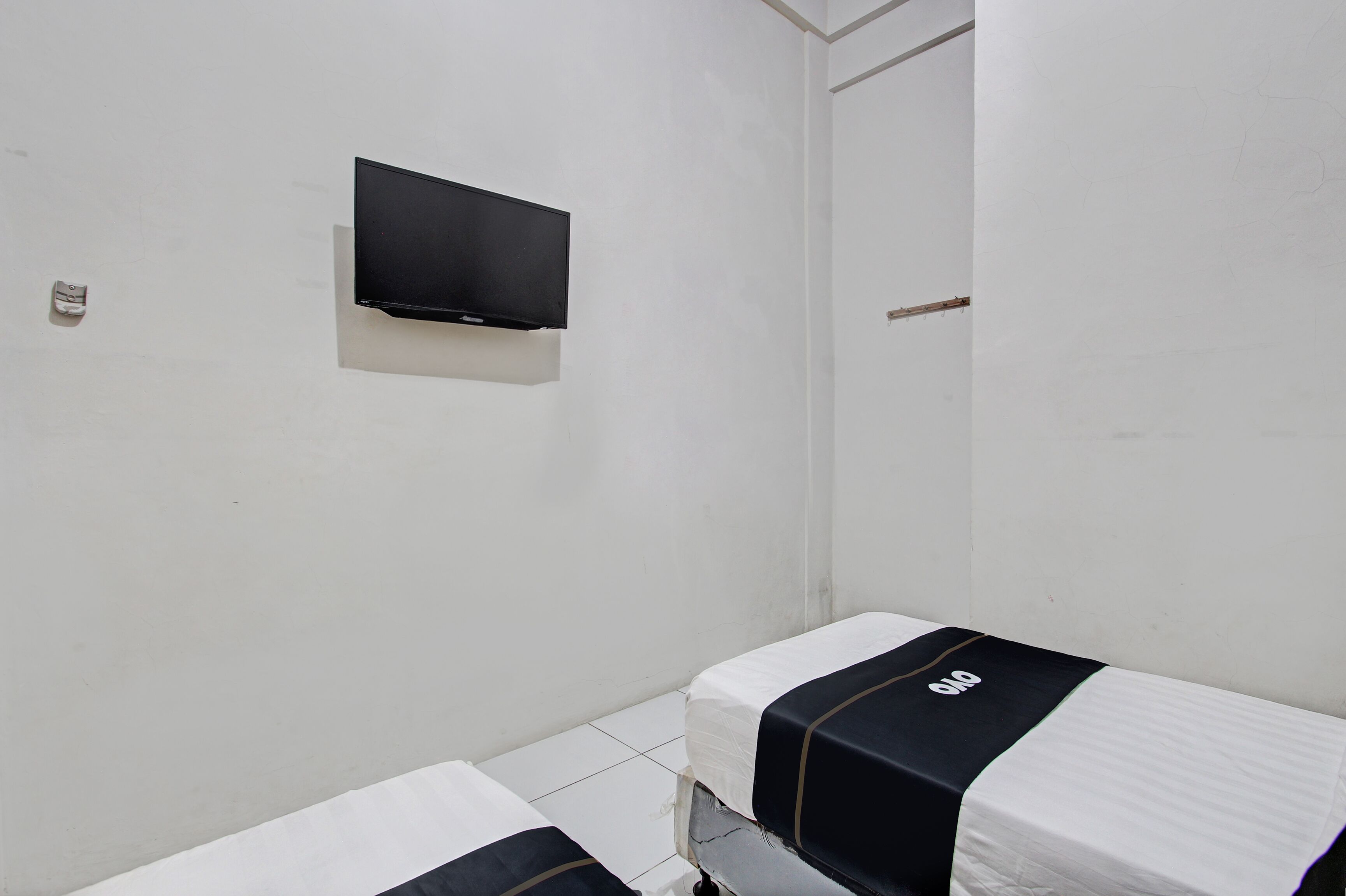 A small, clean room with two beds, a flat-screen TV mounted on the wall, and a door leading to another room.