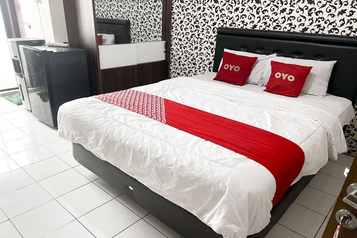 A hotel room with a large bed, two red pillows, a white and red bedspread, and a black headboard.