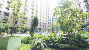 Un immeuble résidentiel de grande hauteur doté de balcons, d’une aire de jeux et d’une végétation luxuriante au premier plan.
