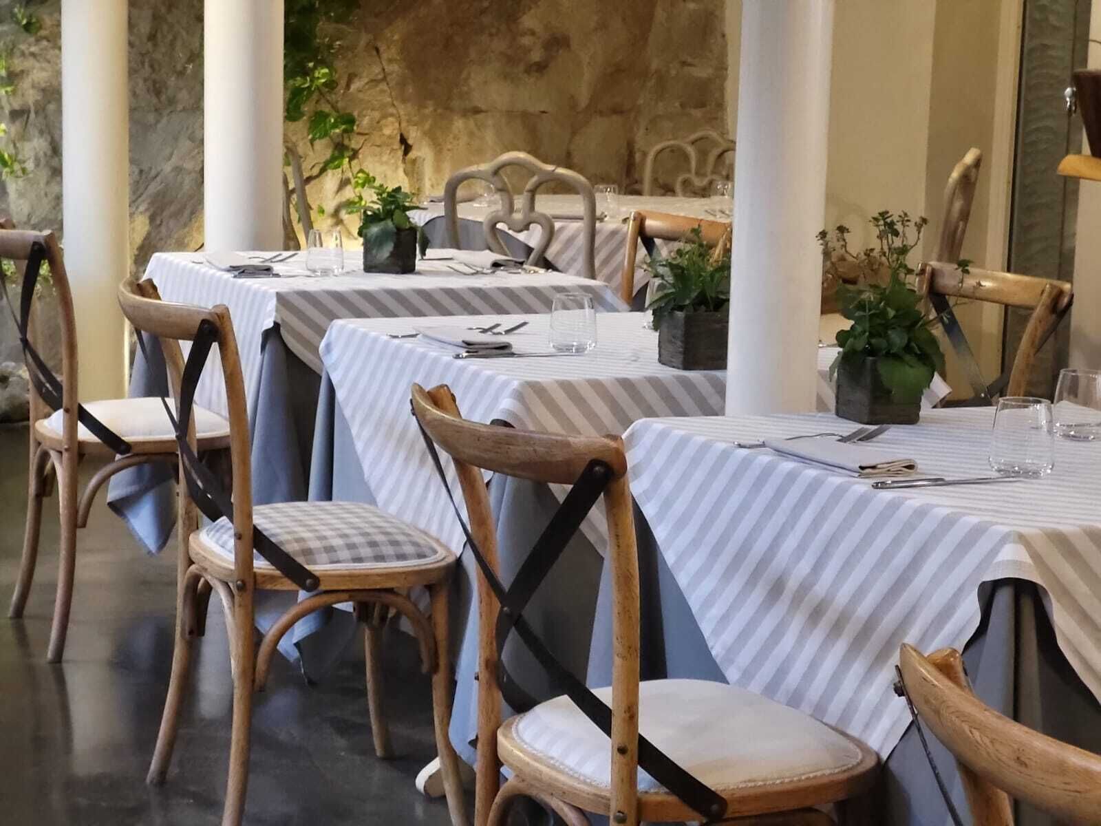 Een restaurant met gedekte tafels, houten stoelen en potplanten.