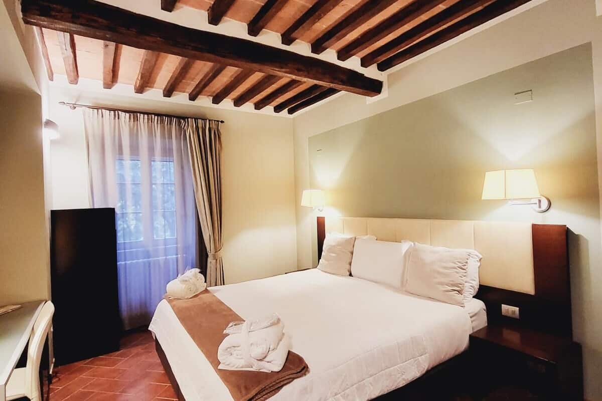 A hotel room with a large bed, wooden ceiling beams, a desk, and a chair.