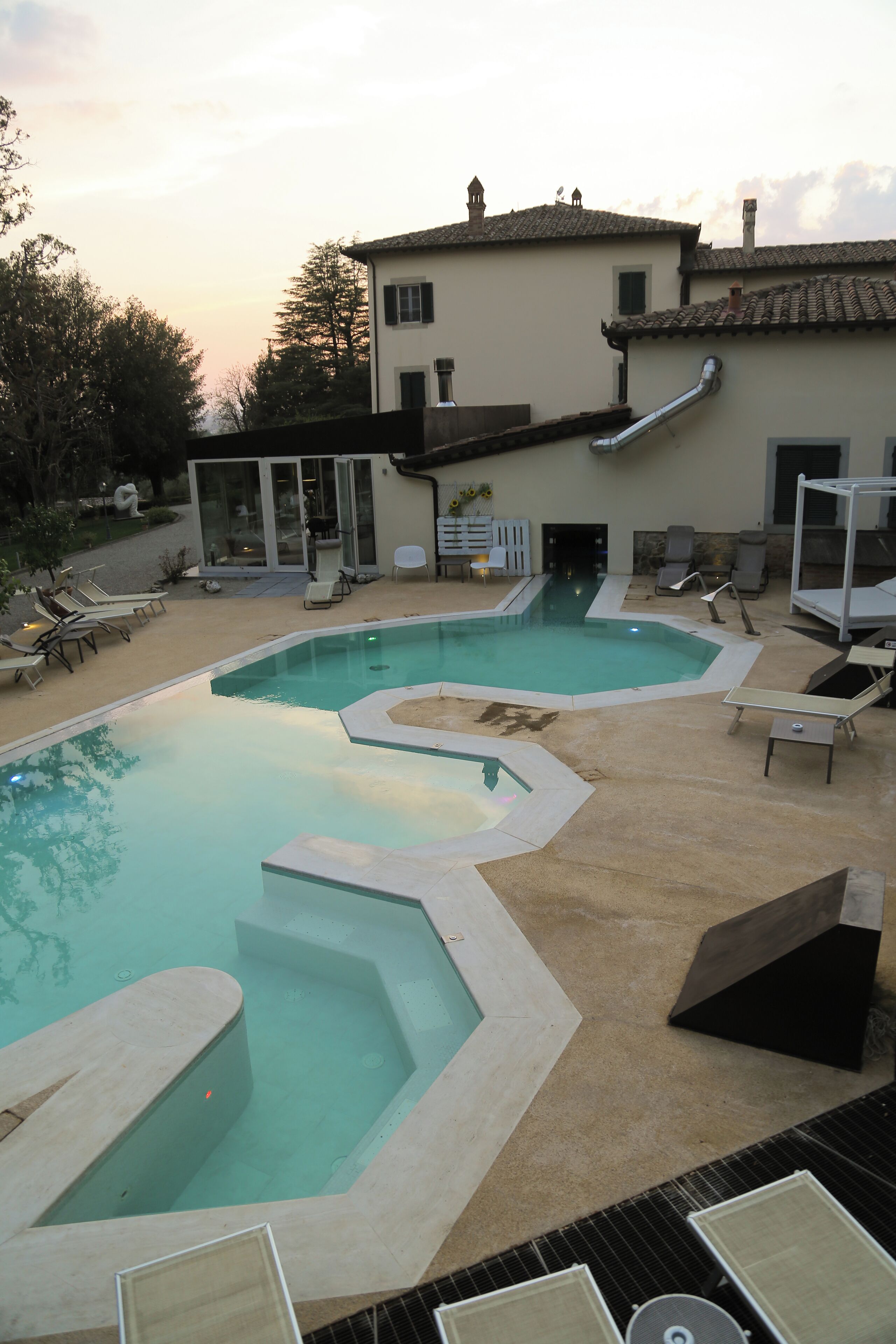 A swimming pool with a unique design, surrounded by lounge chairs and a building with a tiled roof.