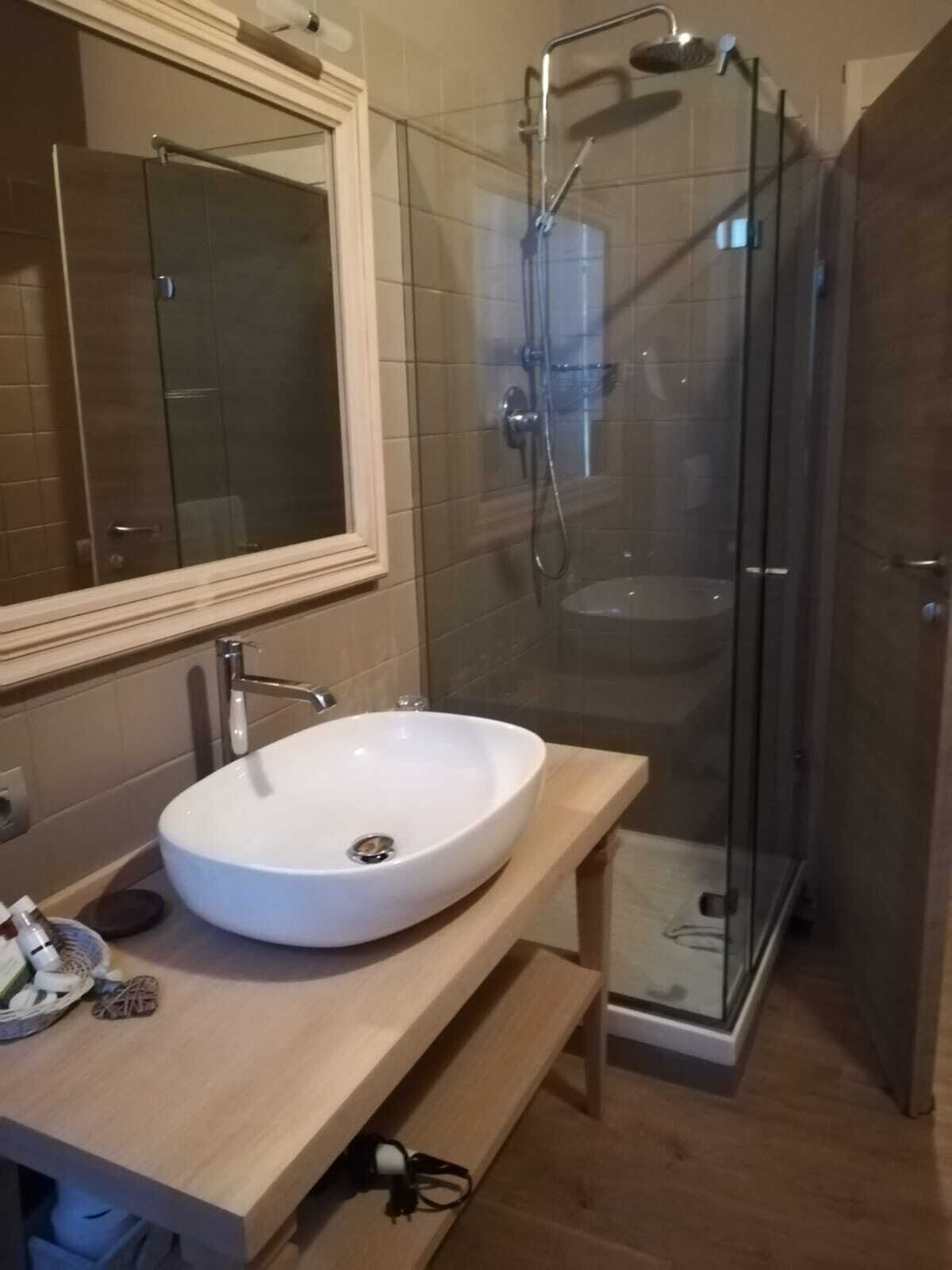 Un baño con lavamanos blanco, espejo y ducha con mampara de vidrio.