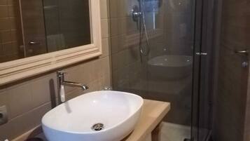 Un baño con lavamanos blanco, espejo y ducha con mampara de vidrio.