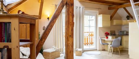 A cozy loft-style room with exposed wooden beams, a loft bed, a small kitchen area, and a dining table with chairs.