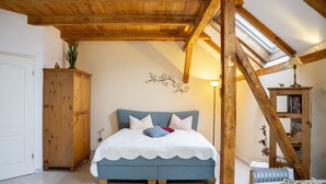 Un dormitorio con cama, vigas de madera en el techo, tragaluz, armario de madera y radiador.