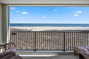 Een balkon met rieten meubilair, uitzicht op het strand en een heldere lucht.