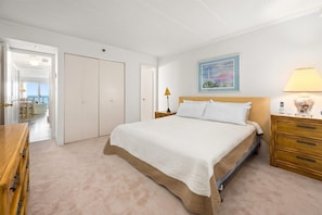 Een slaapkamer met een bed, nachtkastjes, een lamp, een schilderij en uitzicht op een balkon.