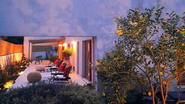 Un espace extérieur moderne, aménagé avec un patio couvert, des plantes en pot et une entrée bien éclairée.