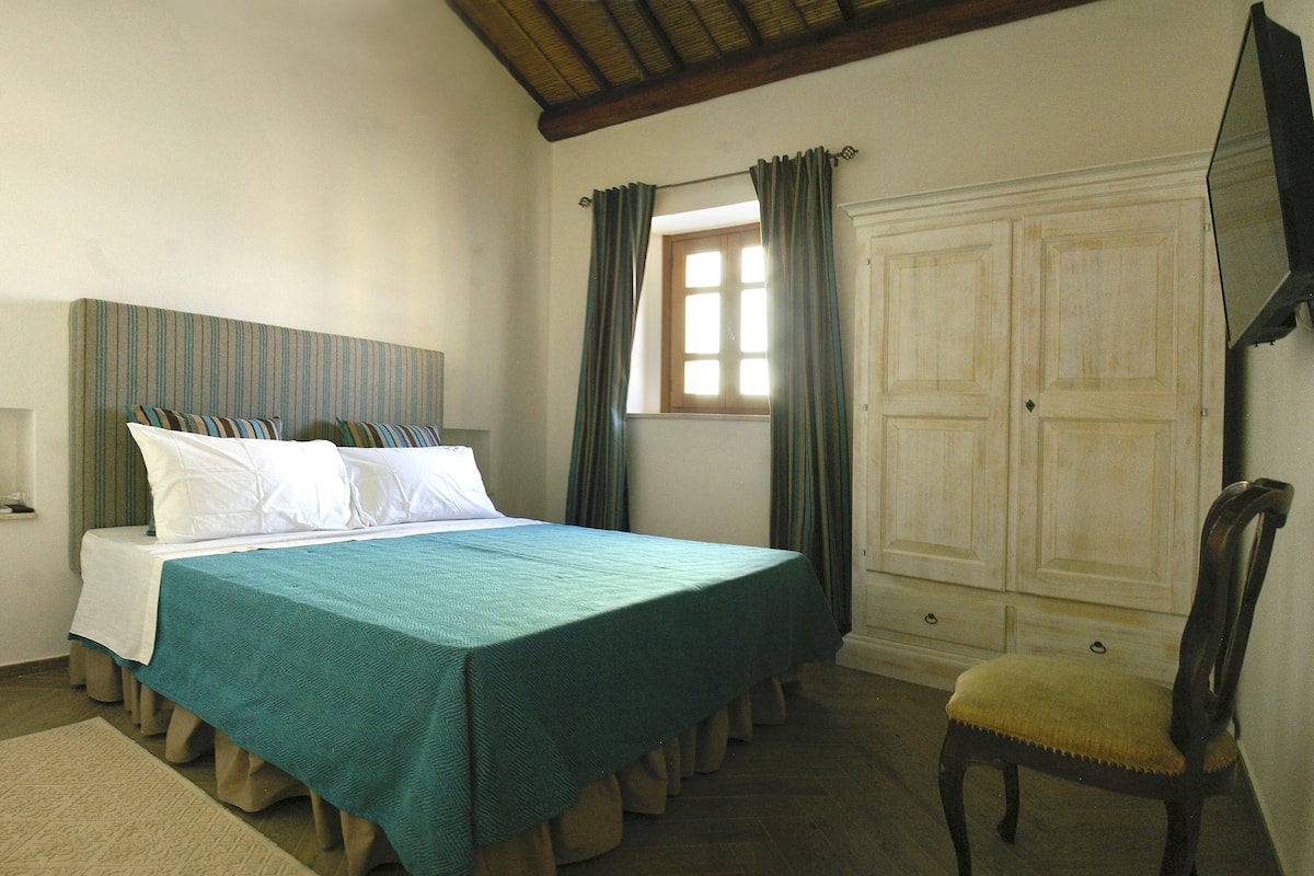 Ein Schlafzimmer mit einem Bett, einem Sessel, einem Kleiderschrank und einem Fenster mit Vorhängen.