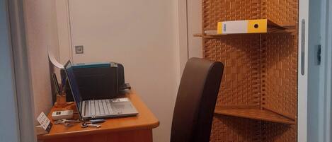 Ein kleiner Arbeitsraum mit Schreibtisch, Stuhl, Laptop und Aktenschrank.