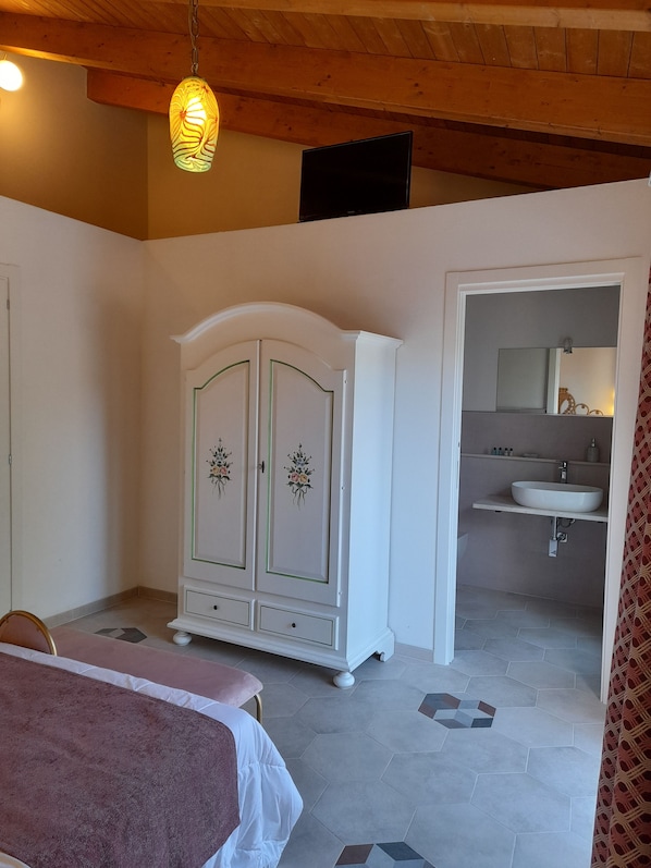 A bedroom with a bed, a wardrobe, and a bathroom with a sink. - Girasole Boutique B&B (Riola Sardo)