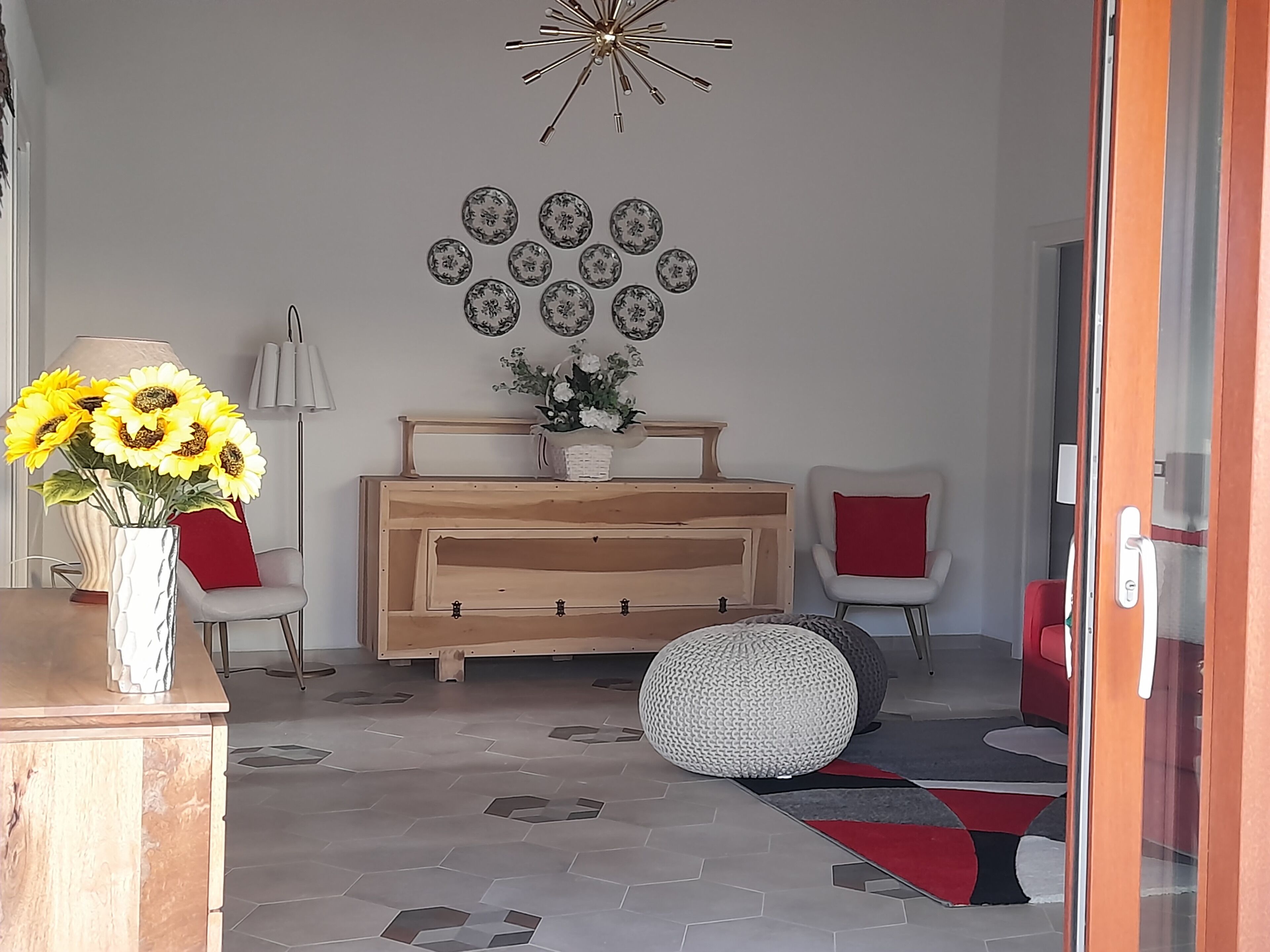 A living room with a wooden cabinet, a vase with sunflowers, a wall-mounted light fixture, and a red chair.