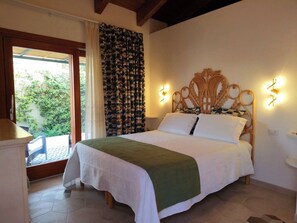 A bedroom with a bed, a window with curtains, a nightstand, and a view of greenery outside.