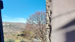 A view through a window with a stone wall, a tree, and a fenced garden area. - In the heart of a medieval French village. One bed apartment. Pet friendly (Cipières)