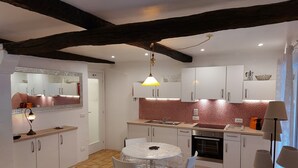 A compact kitchen with white cabinets, a tiled backsplash, and a dining table with chairs. - In the heart of a medieval French village. One bed apartment. Pet friendly (Cipières)