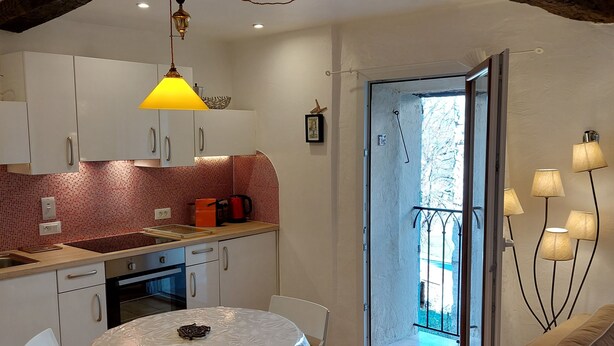 A kitchen with white cabinets, a tiled backsplash, and a round table with chairs. There is a sliding glass door leading to a balcony. - In the heart of a medieval French village. One bed apartment. Pet friendly (Cipières)