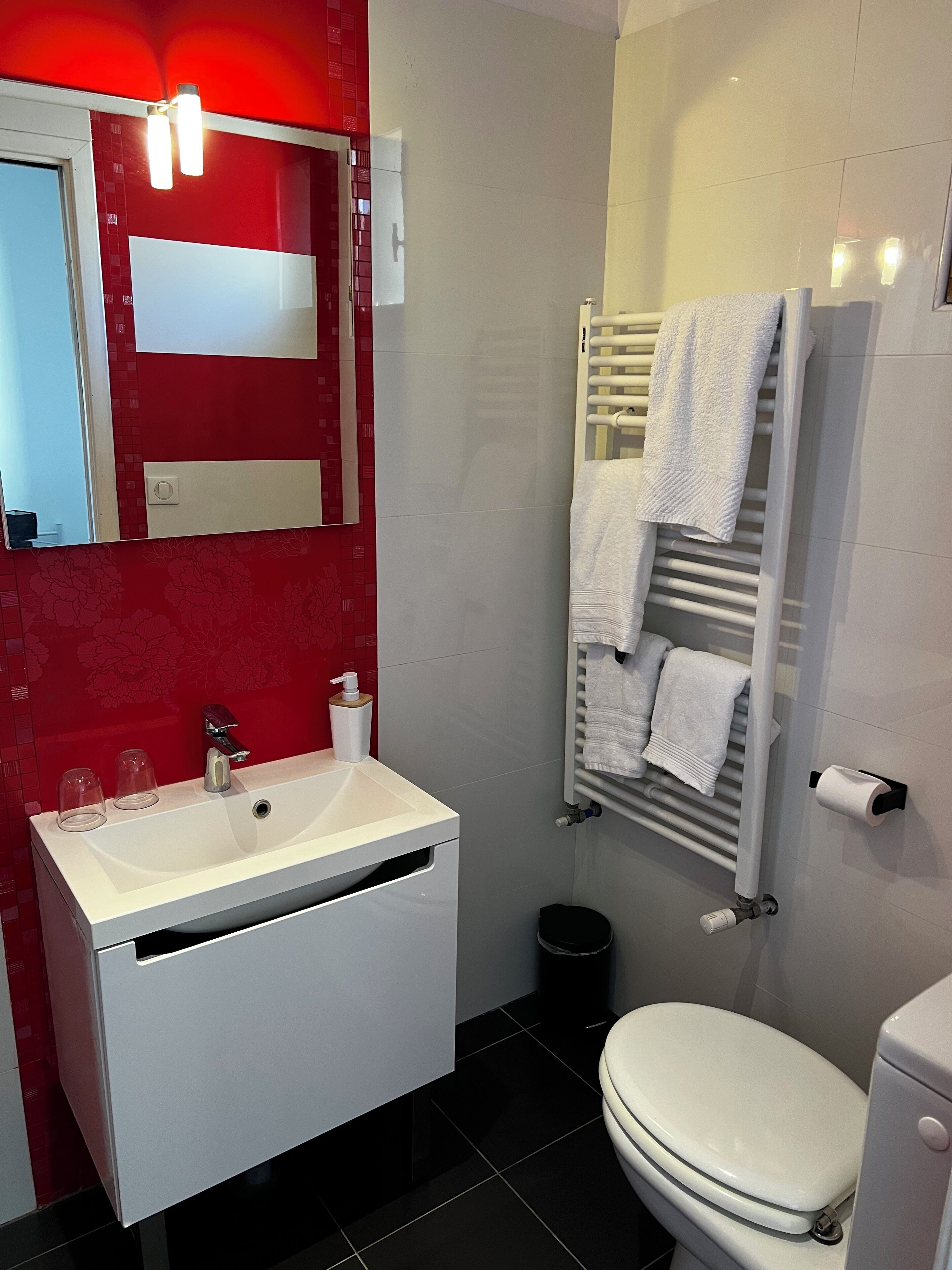 A modern bathroom with a white sink, a mirror, a towel rack, and a toilet.